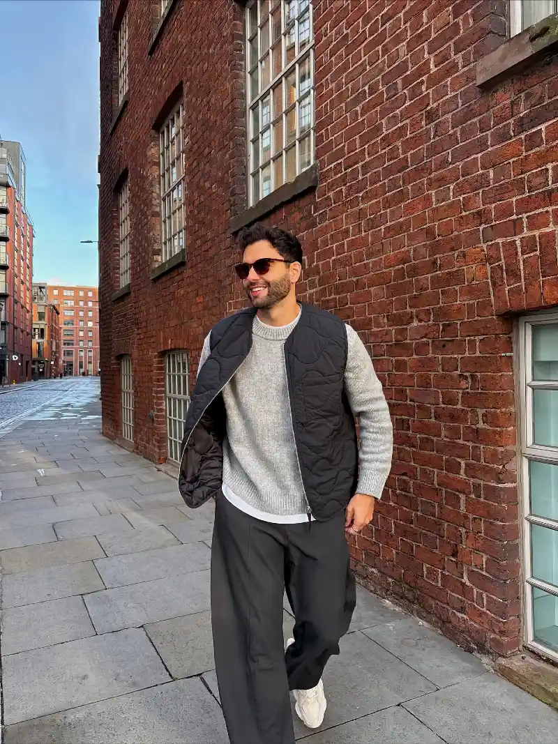 Black Quilted Vest over Grey Crewneck with Loose Charcoal Trousers